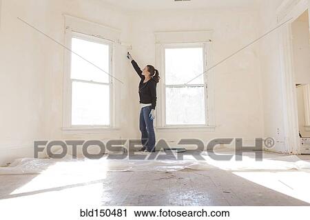 Stock Image - Mixed race woman painting walls of new home. Fotosearch