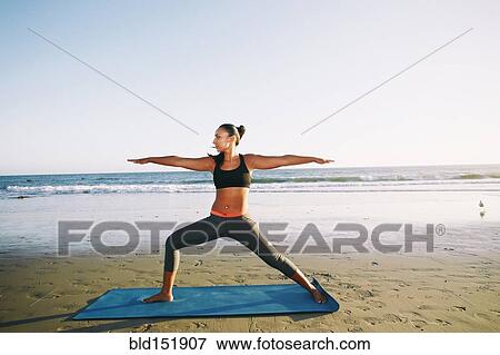 Stock Photo - Mixed race woman practicing yoga on beach. Fotosearch