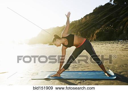 Stock Photo - Mixed race woman practicing yoga on beach. Fotosearch