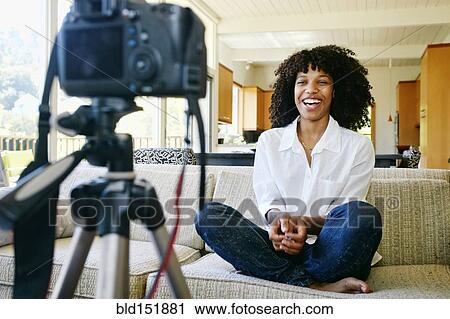 Stock Image - Mixed race woman recording video of herself in living room. Fotosearch