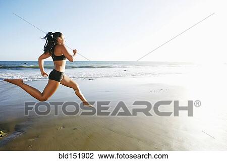 Stock Image - Mixed race woman running on beach. Fotosearch
