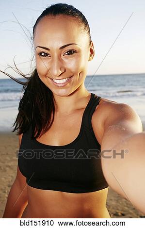 Stock Image - Mixed race woman taking cell phone selfie on beach. Fotosearch