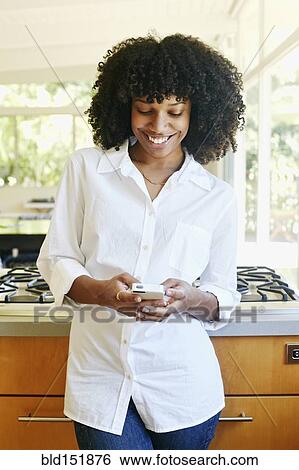 Stock Photograph - Mixed race woman using cell phone in domestic kitchen. Fotosearch