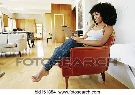Mixed race woman using digital tablet in armchair View Large Photo Image Picture - Mixed race woman using digital tablet in armchair. Fotosearch