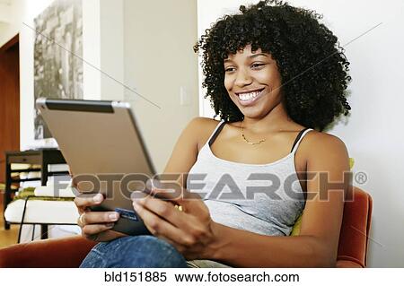 Stock Photography - Mixed race woman using digital tablet in armchair. Fotosearch
