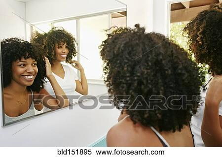 Stock Photography - Mixed race women admiring themselves in mirror. Fotosearch