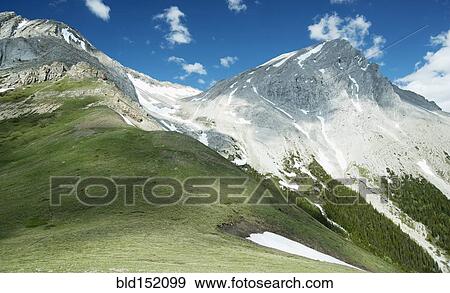 Stock Photo - Mountain peaks with snow and grass under blue sky. Fotosearch