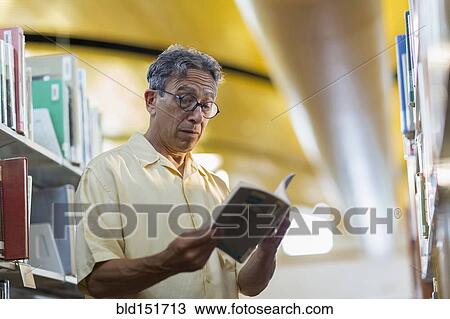 Stock Image - Older Caucasian man reading book in library. Fotosearch