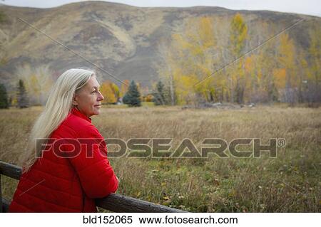 Stock Photography - Older Caucasian woman leaning on wooden fence. Fotosearch