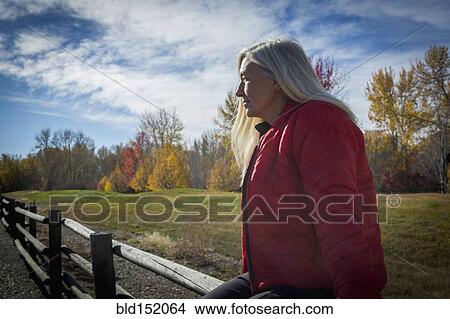 Picture - Older Caucasian woman sitting on wooden fence. Fotosearch