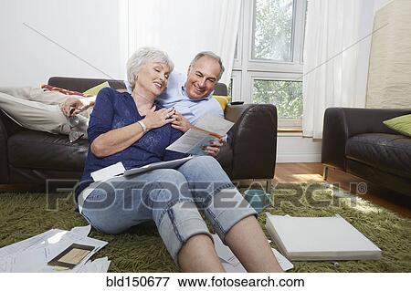 Older couple looking at photographs in living room View Large Photo Image Stock Photo - Older couple looking at photographs in living room. Fotosearch