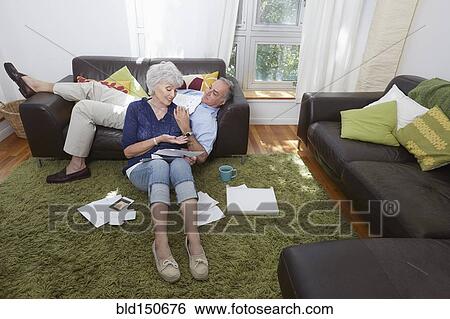 Stock Photograph - Older couple looking at photographs in living room. Fotosearch