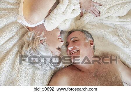Stock Image - Older couple smiling at each other in bed. Fotosearch