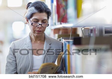 Stock Photo - Older Hispanic woman reading book in library. Fotosearch