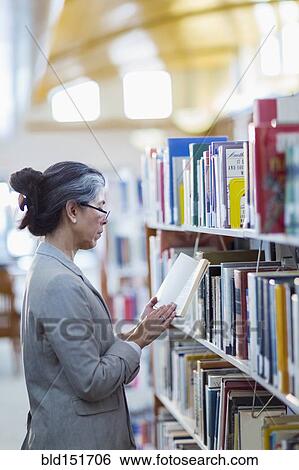 Stock Photograph - Older Hispanic woman reading book in library. Fotosearch
