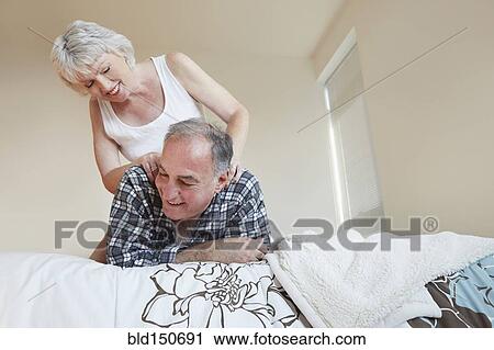 Stock Image - Older woman giving husband back massage on bed. Fotosearch