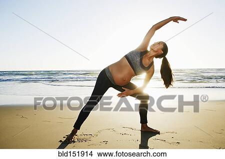 Picture - Pregnant Hispanic woman practicing yoga on beach. Fotosearch