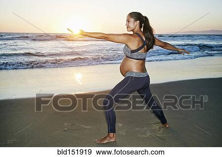 Stock Photo - Pregnant Hispanic woman practicing yoga on beach. Fotosearch