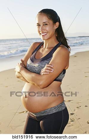 Stock Photograph - Pregnant Hispanic woman smiling on beach. Fotosearch