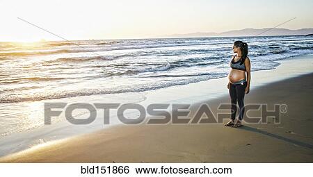 Stock Photograph - Pregnant Hispanic woman standing on beach. Fotosearch