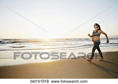 Stock Photo - Pregnant Hispanic woman walking on beach. Fotosearch
