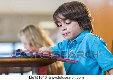 Stock Image - Student reading book at desk. Fotosearch