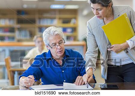 Teacher helping adult student in library View Large Photo Image Stock Image - Teacher helping adult student in library. Fotosearch
