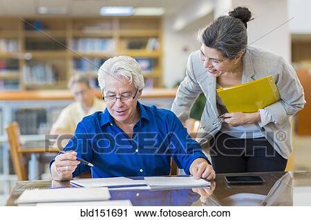 Teacher helping adult student in library View Large Photo Image Stock Image - Teacher helping adult student in library. Fotosearch