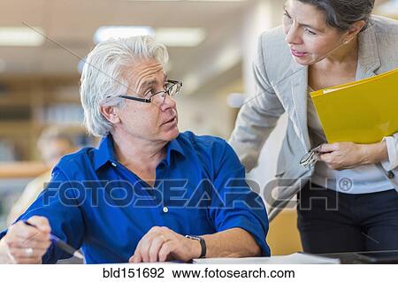 Teacher helping adult student in library View Large Photo Image Stock Image - Teacher helping adult student in library. Fotosearch