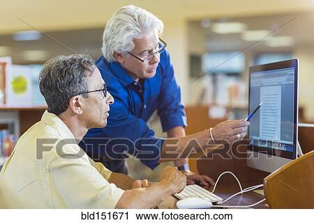 Teacher helping adult student use computer in library View Large Photo Image Stock Image - Teacher helping adult student use computer in library. Fotosearch