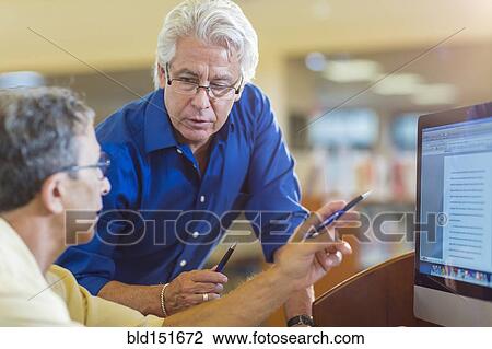 Stock Image - Teacher helping adult student use computer in library. Fotosearch
