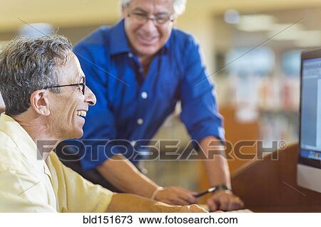 Stock Image - Teacher helping adult student use computer in library. Fotosearch