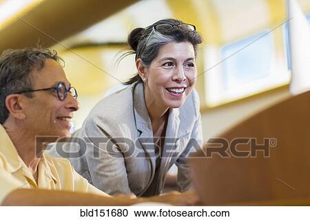 Stock Image - Teacher helping adult student use computer in library. Fotosearch