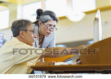Stock Photo - Teacher helping adult student use computer in library. Fotosearch