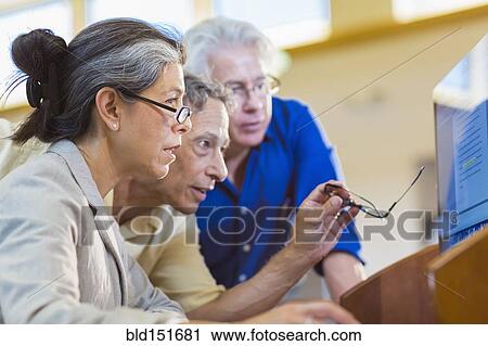Teacher helping adult students use computer in library View Large Photo Image Stock Image - Teacher helping adult students use computer in library. Fotosearch