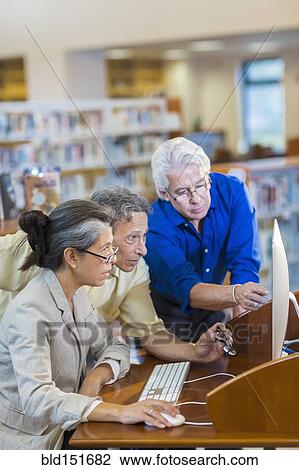 Teacher helping adult students use computer in library View Large Photo Image Stock Image - Teacher helping adult students use computer in library. Fotosearch