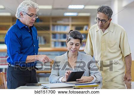 Stock Image - Teacher helping adult students use digital tablet in library. Fotosearch