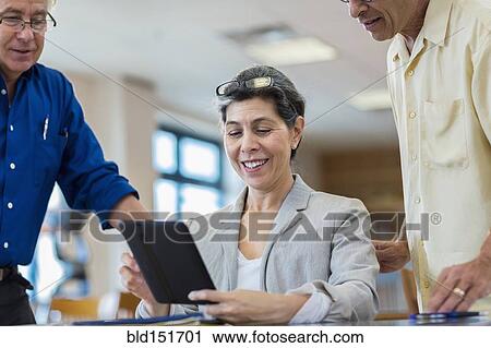 Stock Image - Teacher helping adult students use digital tablet in library. Fotosearch