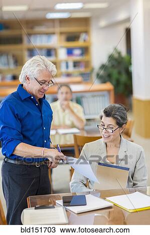 Stock Image - Teacher helping adult students use digital tablet in library. Fotosearch