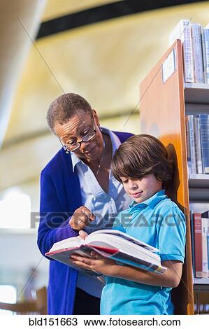 Stock Image - Teacher helping student in library. Fotosearch