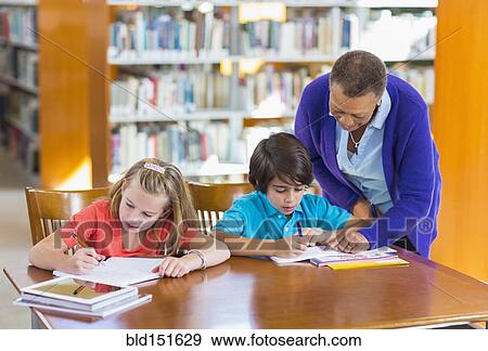 Teacher helping student in library View Large Photo Image Stock Photo - Teacher helping student in library. Fotosearch