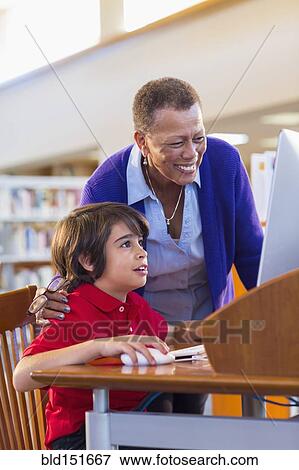 Teacher helping student use computer in library View Large Photo Image Stock Photo - Teacher helping student use computer in library. Fotosearch