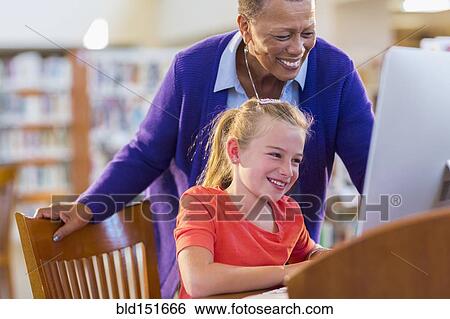 Stock Photograph - Teacher helping student use computer in library. Fotosearch