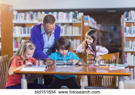 Teacher helping student use digital tablet in library View Large Photo Image Picture - Teacher helping student use digital tablet in library. Fotosearch