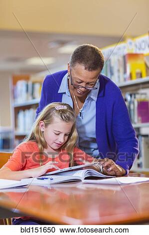 Stock Image - Teacher helping student use digital tablet in library. Fotosearch