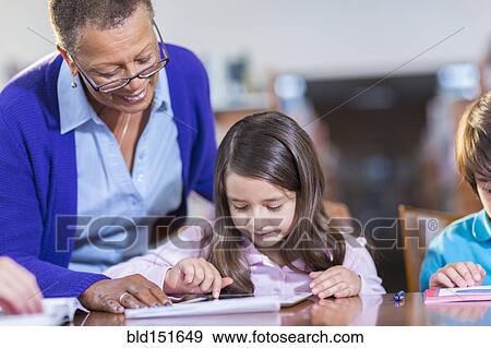 Teacher helping student use digital tablet in library View Large Photo Image Stock Photo - Teacher helping student use digital tablet in library. Fotosearch