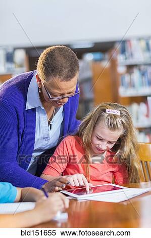Teacher helping student use digital tablet in library View Large Photo Image Stock Photography - Teacher helping student use digital tablet in library. Fotosearch