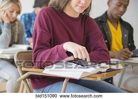 Stock Image - Teenage student using digital tablet on desk in classroom. Fotosearch