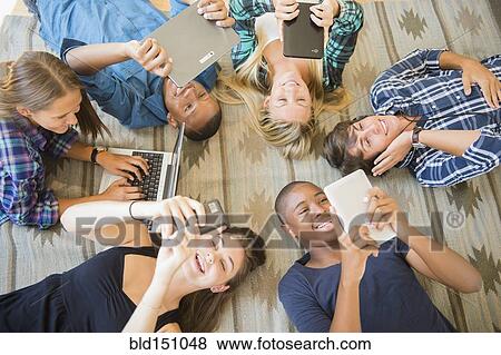 Stock Photo - Teenagers laying on floor using technology. Fotosearch