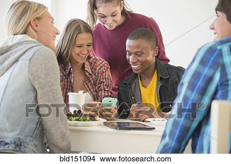 Teenagers using cell phone at table View Large Photo Image Picture - Teenagers using cell phone at table. Fotosearch